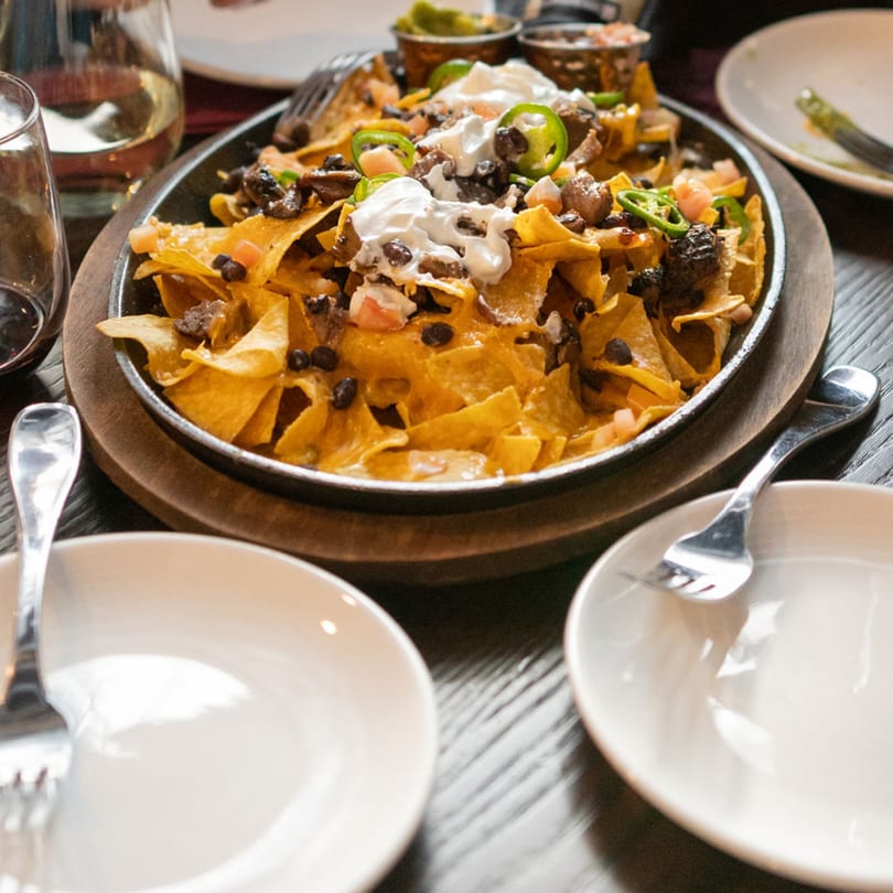 A sizzling platter of nachos with cheese, black beans, meat, sour cream, and jalapeños.