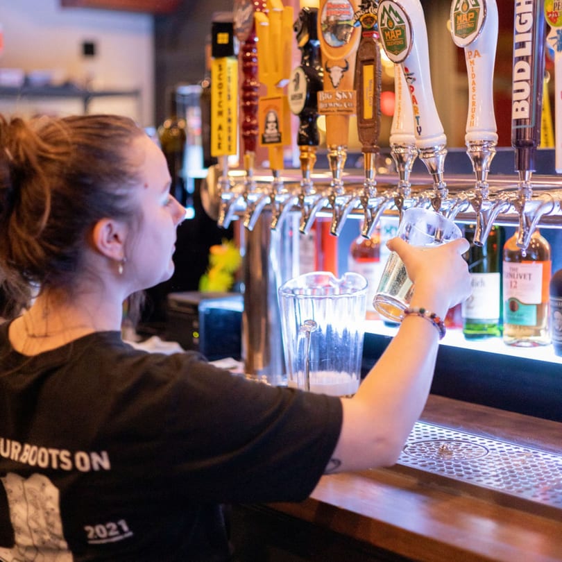 A bartender pours a beer from one of many taps into a glass at a bar.
