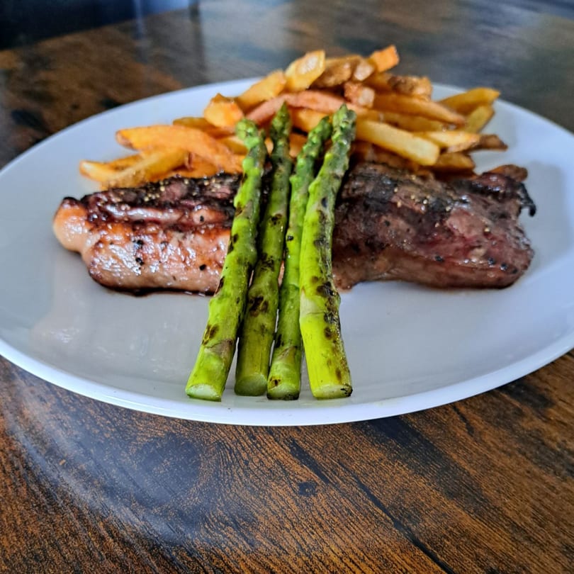 Grilled steak, asparagus spears, and golden french fries on a white plate.