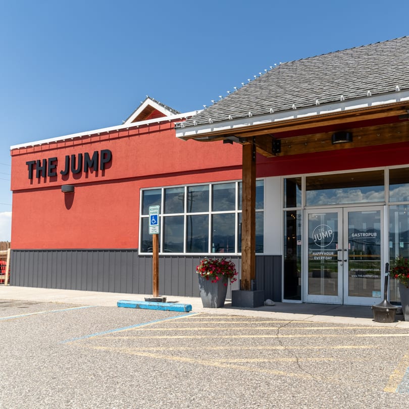 Exterior of The Jump Gastropub, a red building with a gray base, parking lot, and blue sky.