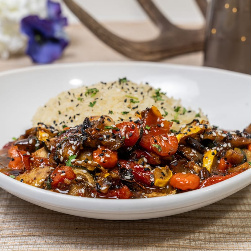 A white bowl of stir-fried vegetables with rice, garnished with sesame seeds and parsley.