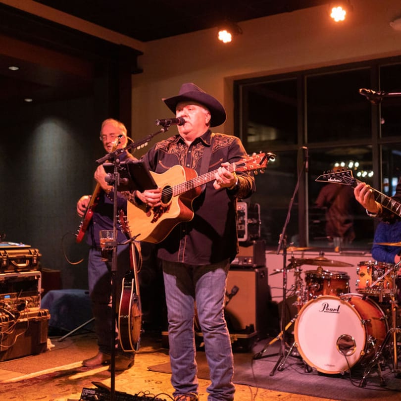 A country band performs live on stage, with the lead singer playing an acoustic guitar.