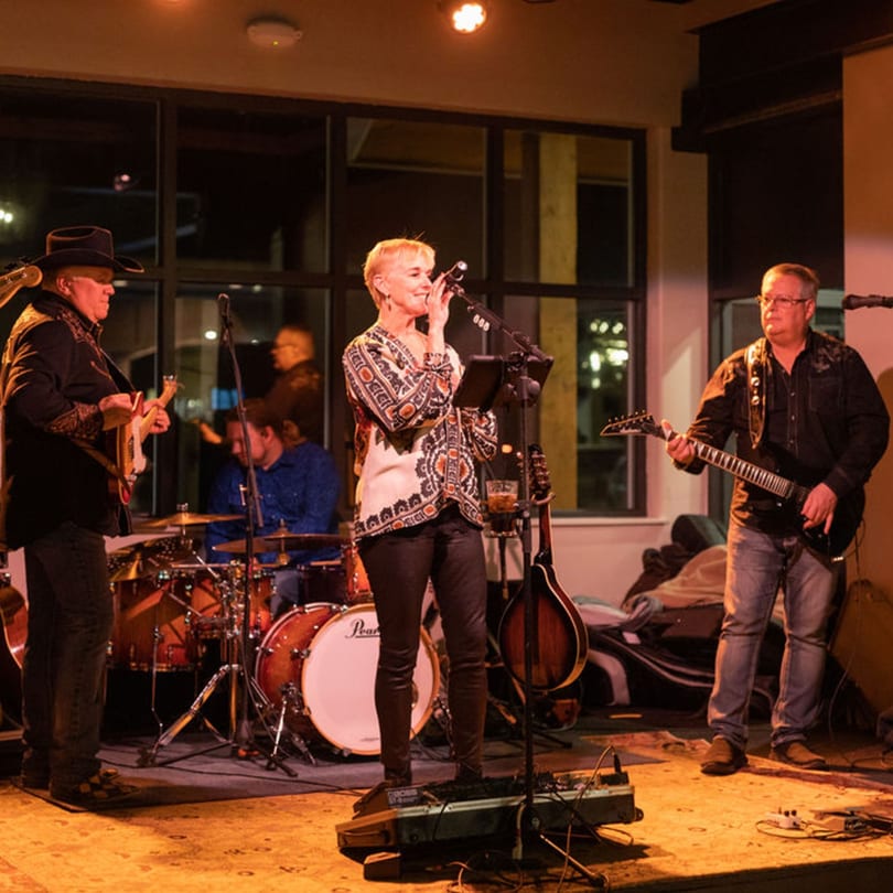 A band performs live on stage, featuring a female vocalist, two guitarists, and a drummer.