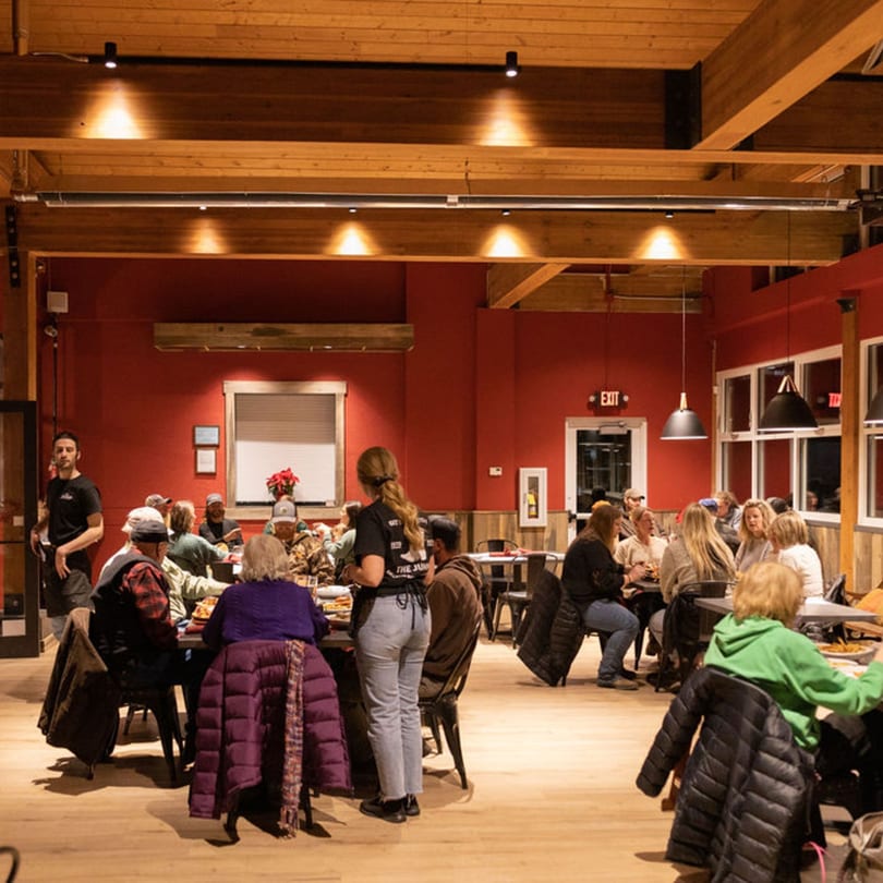 A bustling restaurant interior with red walls, wooden beams, and patrons dining at tables.