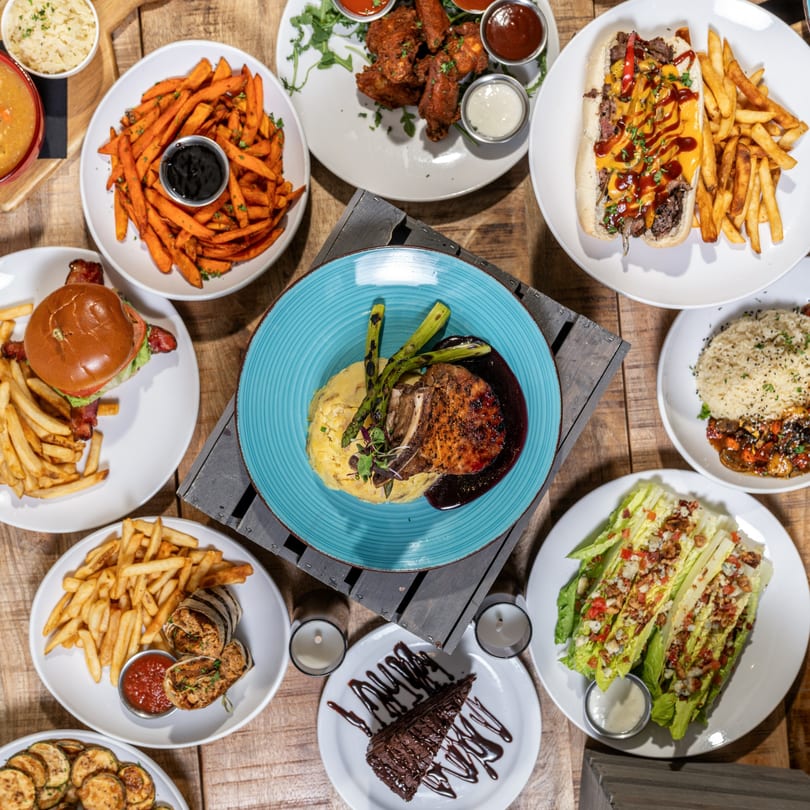 Overhead view of various bar-and-grill dishes, including burgers, fries, wings, and steak.