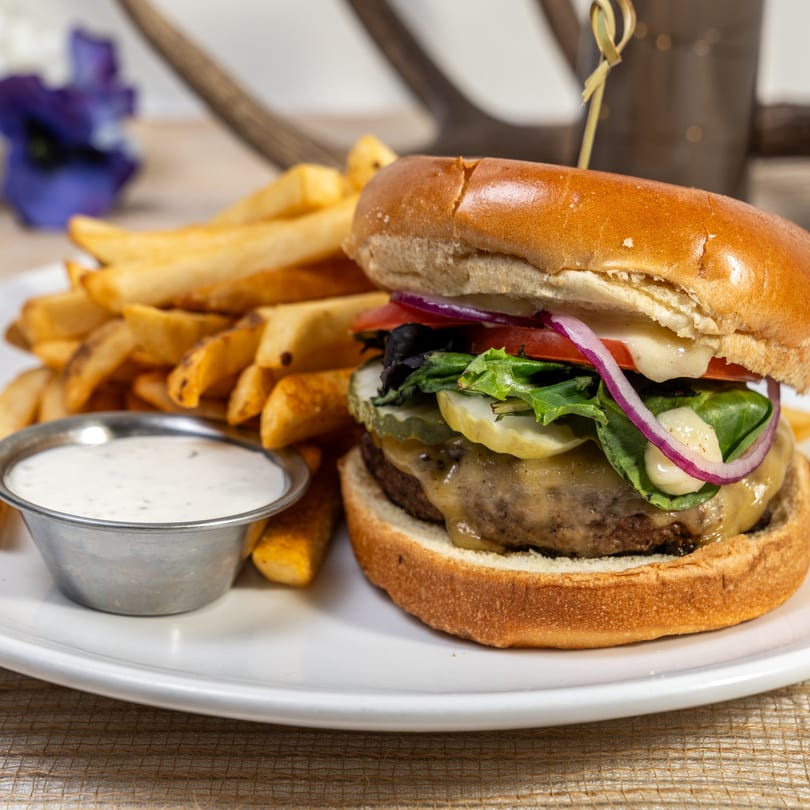 A Jump Restaurant & Bar burger with fries and dipping sauce on a white plate.
