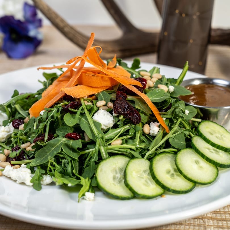 Arugula salad with shaved carrots, dried cranberries, pine nuts, feta, and cucumber slices.