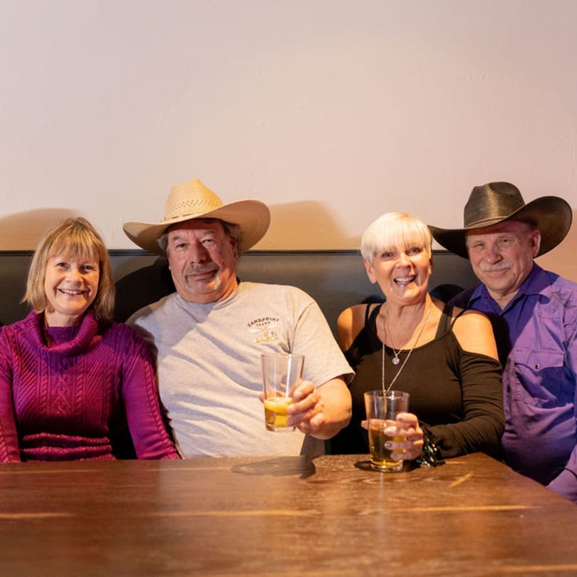Four smiling people, two men in cowboy hats and two women, sitting at a table with drinks.