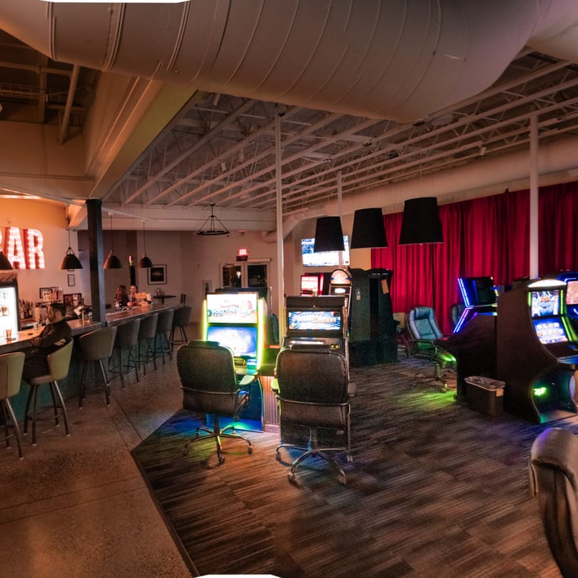 A bar area with patrons and a gaming room with slot machines and red curtains.