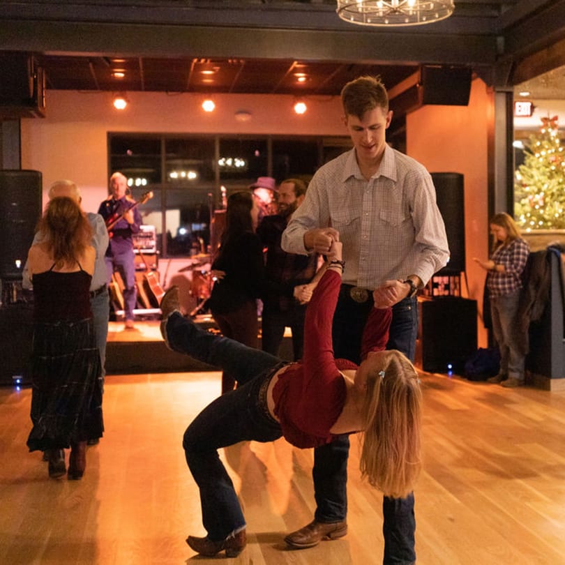 A couple dances in a dip pose on a wooden floor with a band playing in the background.